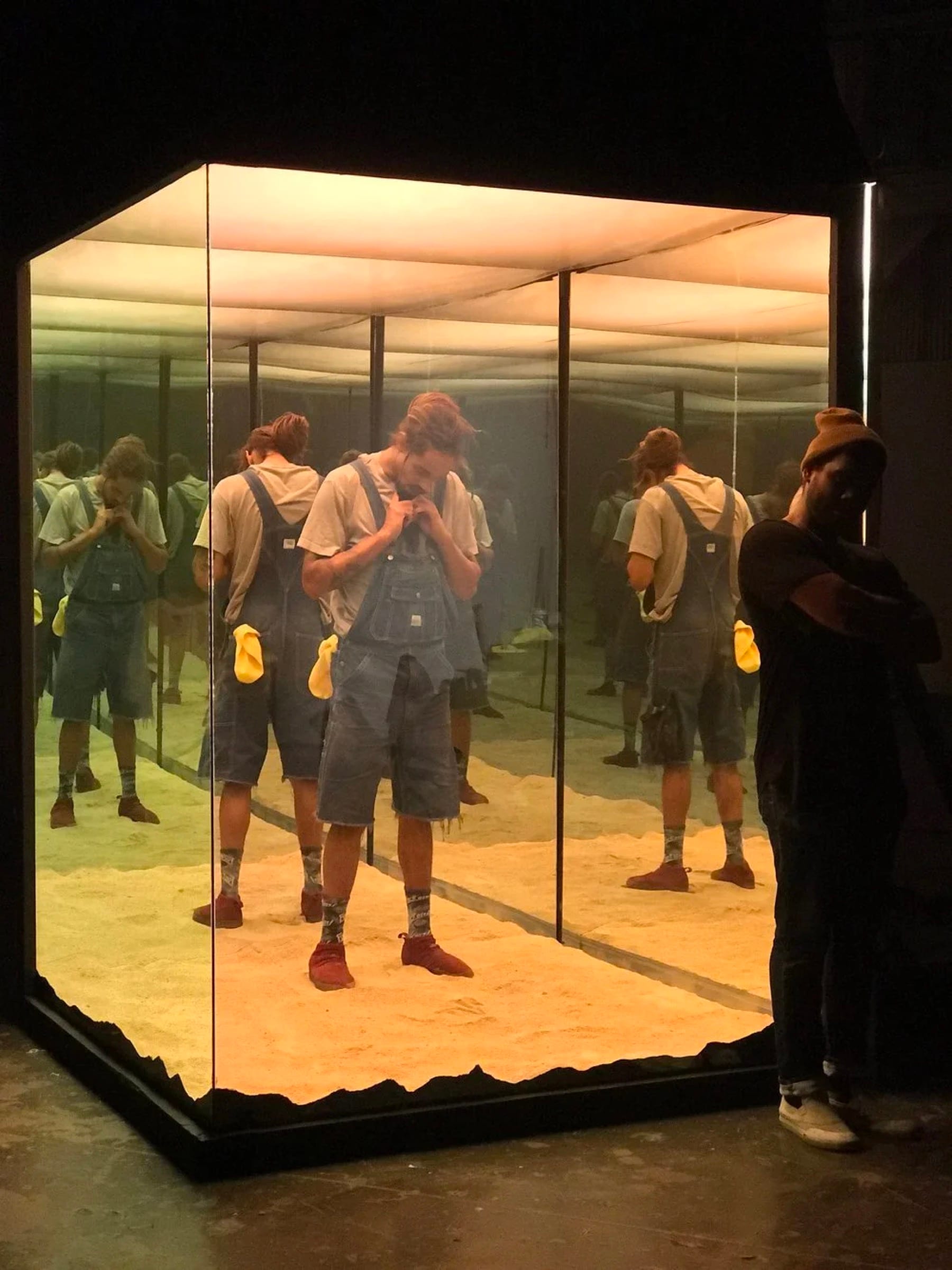 Performer inside an amber-lit mirrored installation with repeated reflections