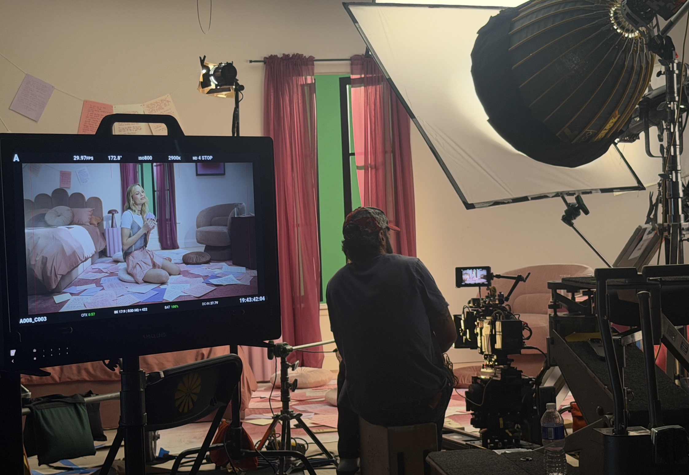 Behind-the-scenes view of the pink bedroom set with the camera crew and studio lighting